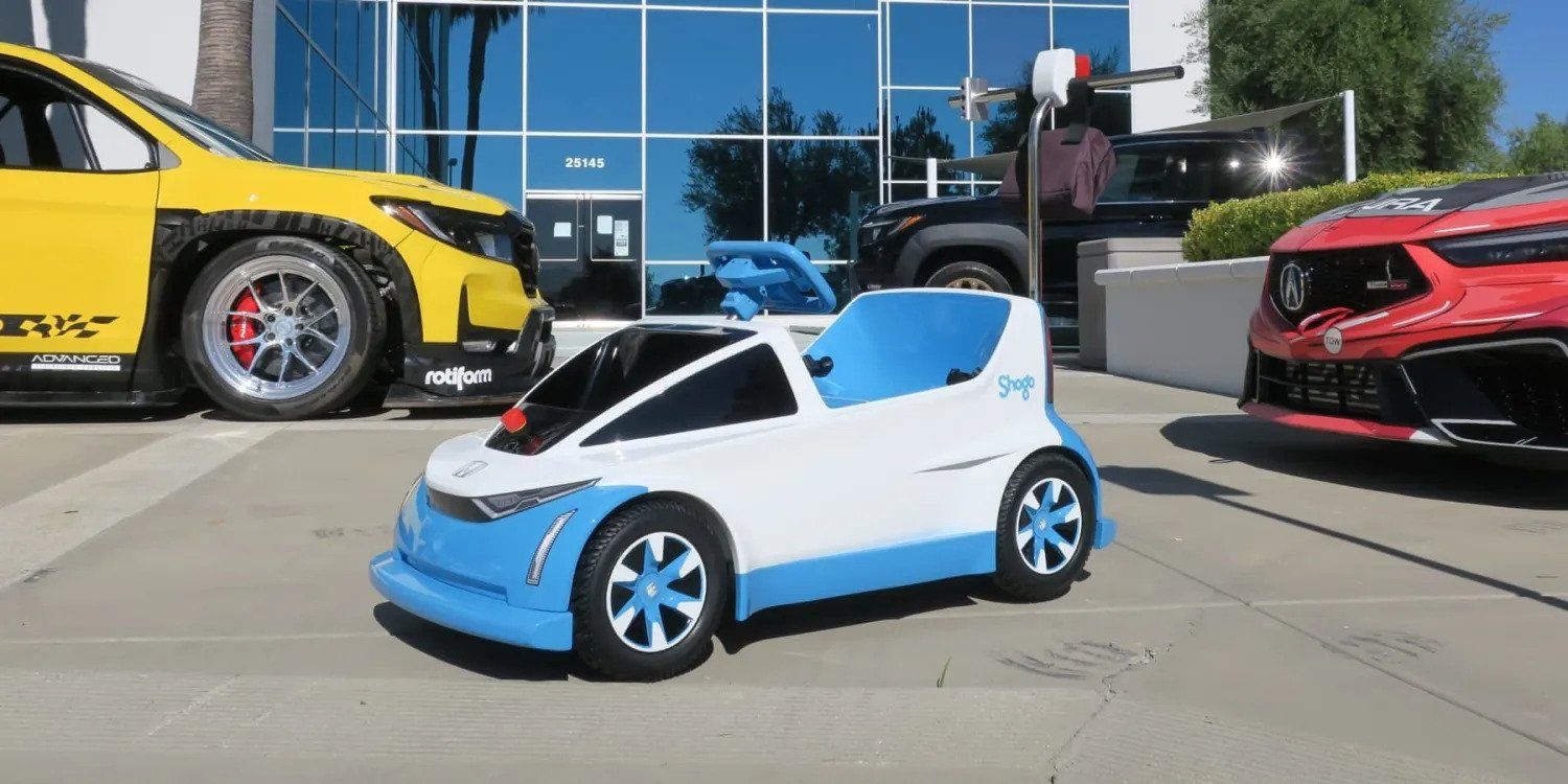 Small blue-and-white toy car displayed outdoors between larger sports cars.