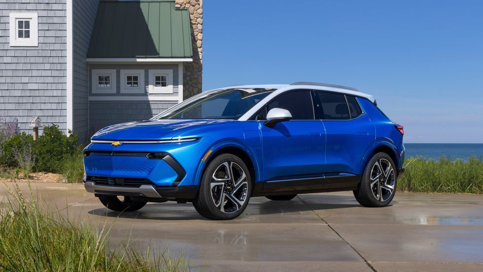 Blue electric SUV parked beside a house near the coast on a sunny day