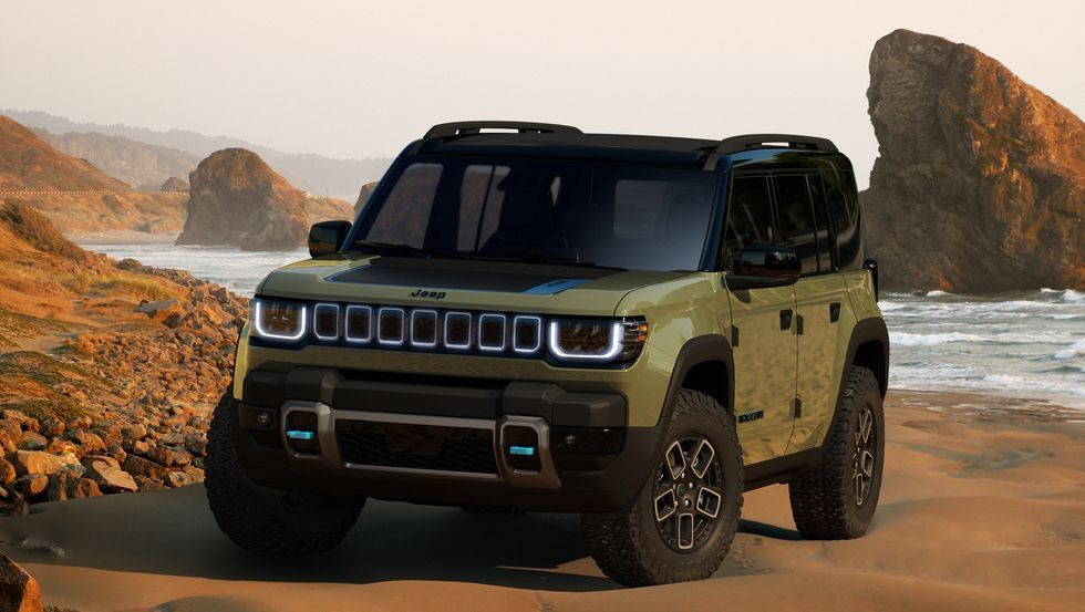 Olive-green SUV on a rocky beach with cliffs and ocean waves in the background