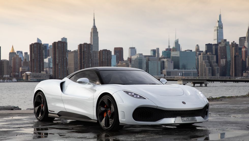 White sports car parked on wet pavement with a city skyline in the background
