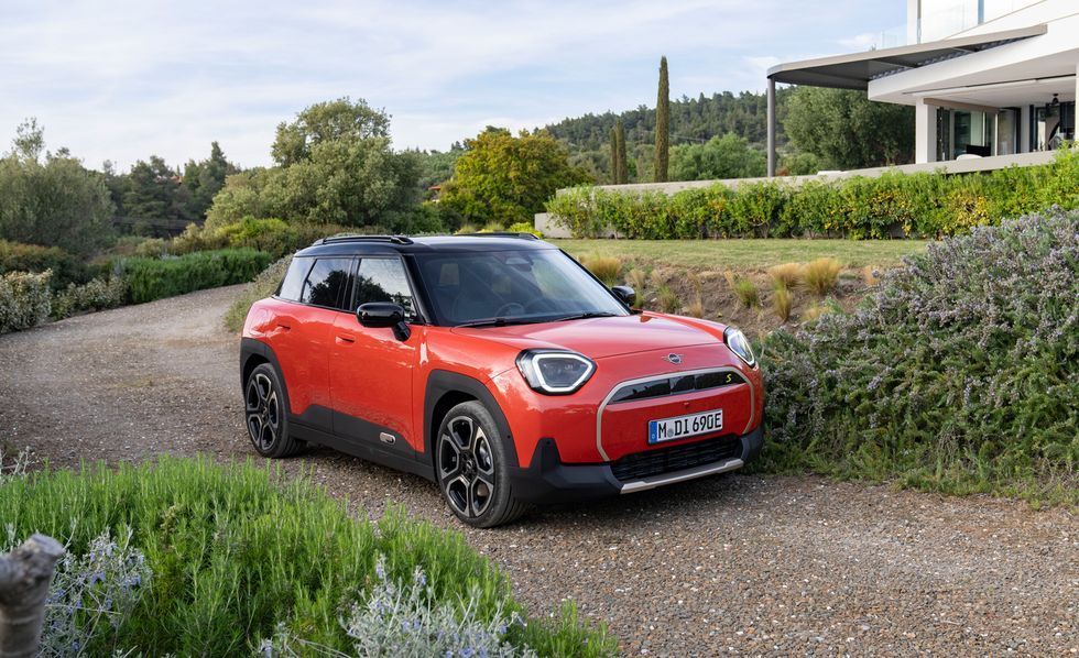Red compact SUV parked on a gravel driveway beside hedges and a modern house