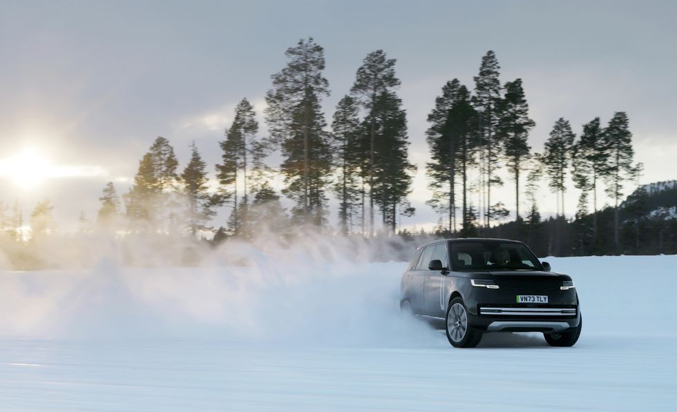 Black SUV driving through snowy fog at sunrise in a pine forest