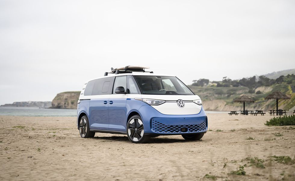 Blue-and-white van parked on a sandy beach near the ocean and cliffs.