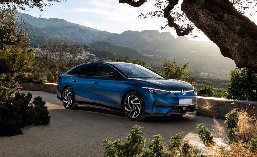 Blue sedan parked on a scenic mountain overlook with trees and distant hills at sunset