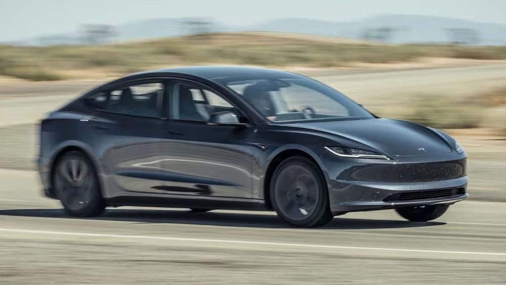 Dark gray sedan driving fast on a road with blurred landscape in the background