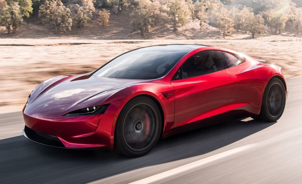 Red sports car driving on a road, with a blurred wooded background.
