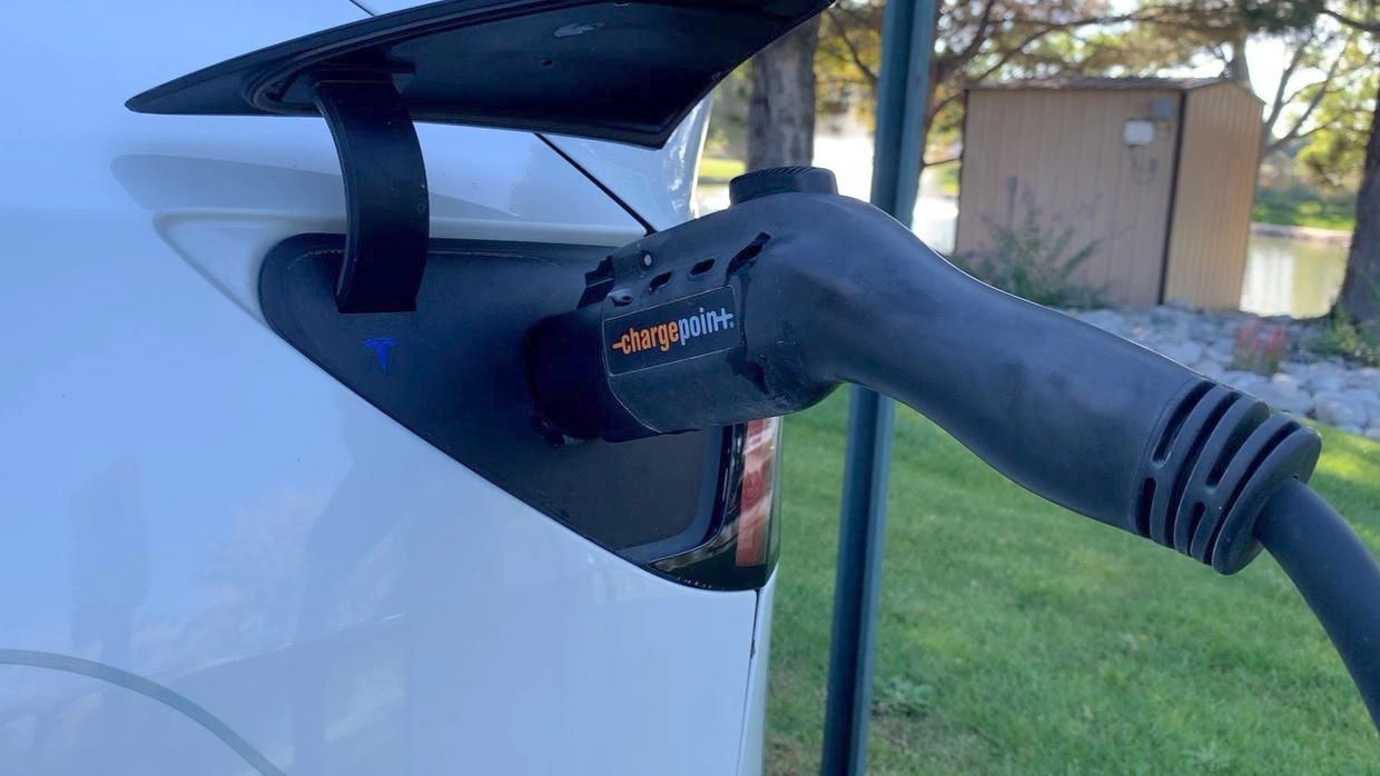 Electric vehicle charging cable plugged into a white car outdoors.