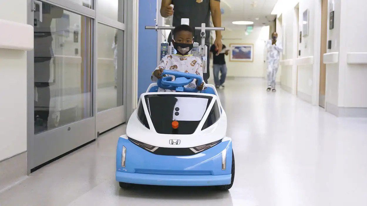 Person riding a blue autonomous hospital cart down a bright hallway