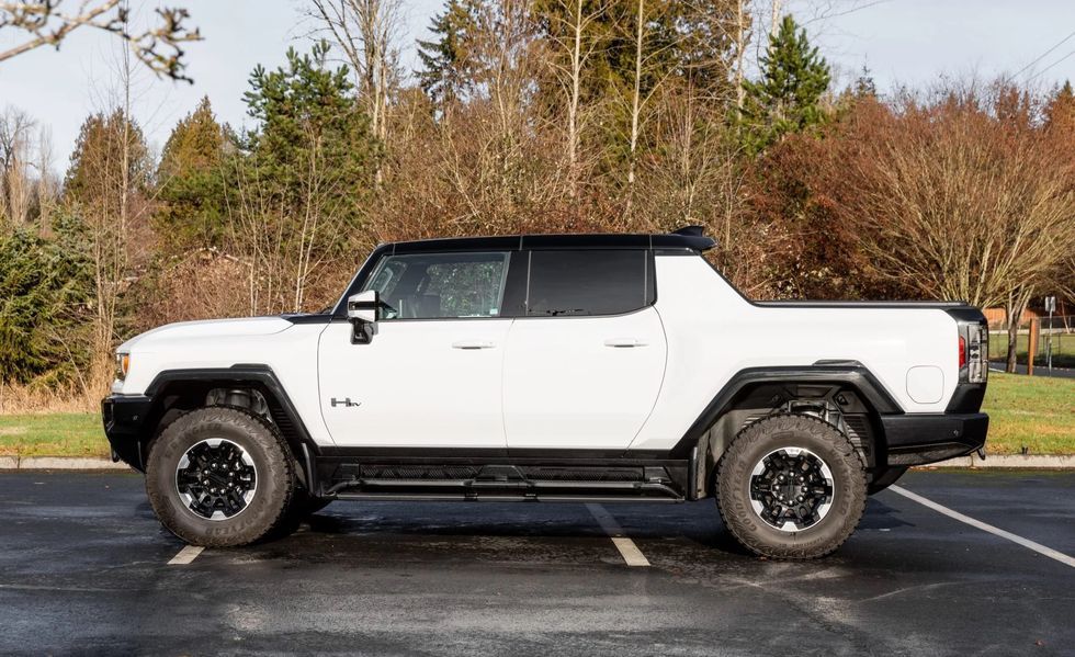 White off-road SUV with black trim parked in a lot beside trees
