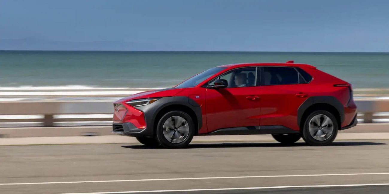 Red SUV driving along a coastal road with ocean and beach in the background