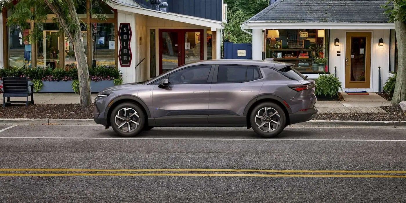 Gray SUV parked on a street in front of small storefronts with blue awnings