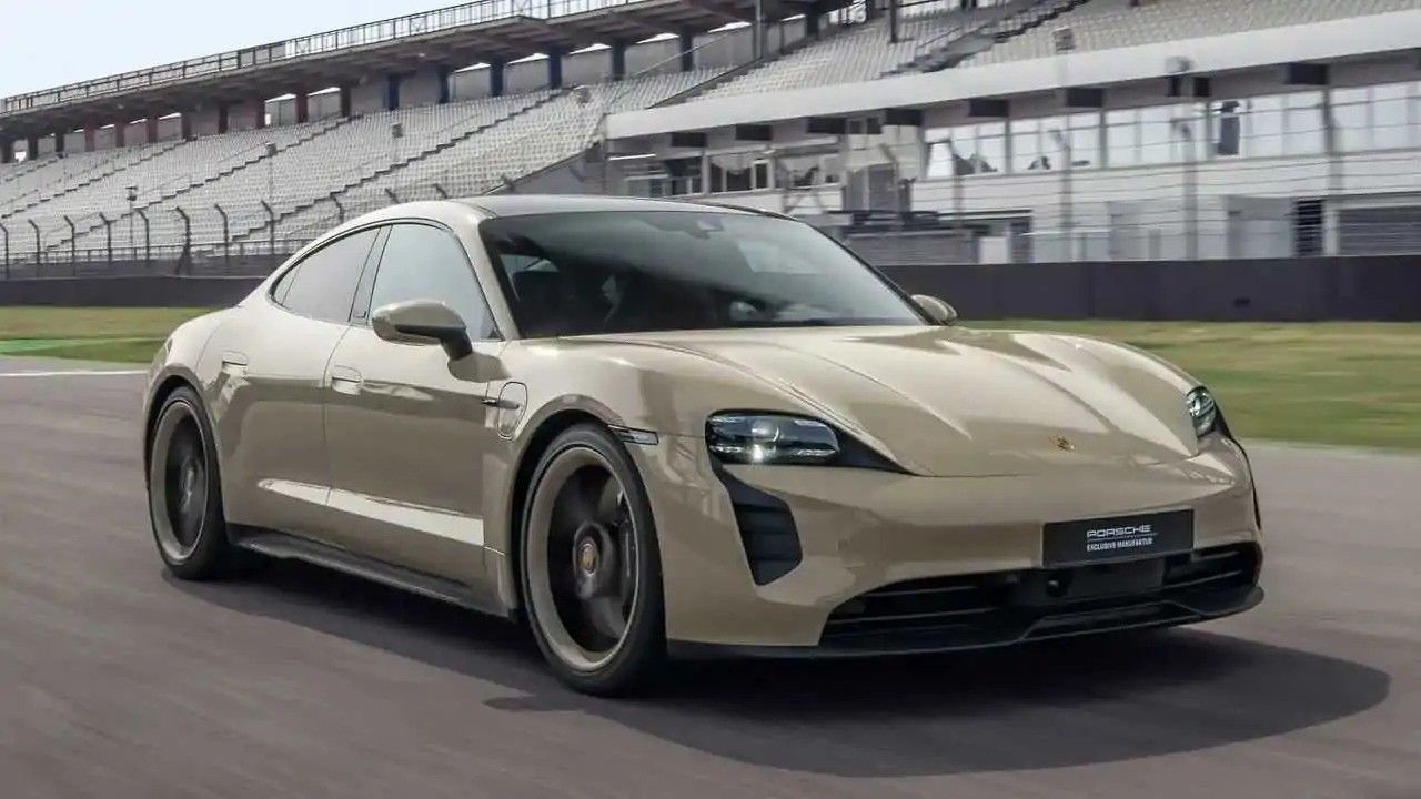 Beige sports car driving on a racetrack, with grandstands in the background.