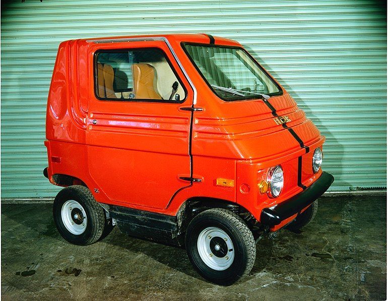 Bright red compact three-wheeled utility vehicle parked in front of a metal garage door