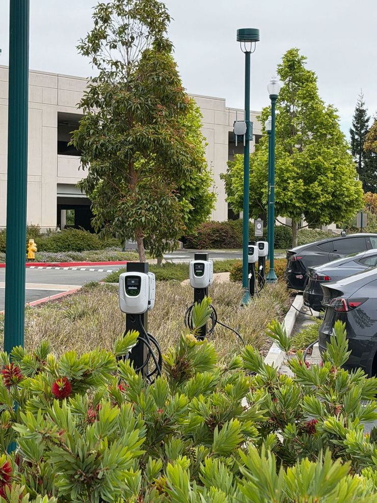 Parking lot with charging stations beside green landscaping and parked cars near an office building