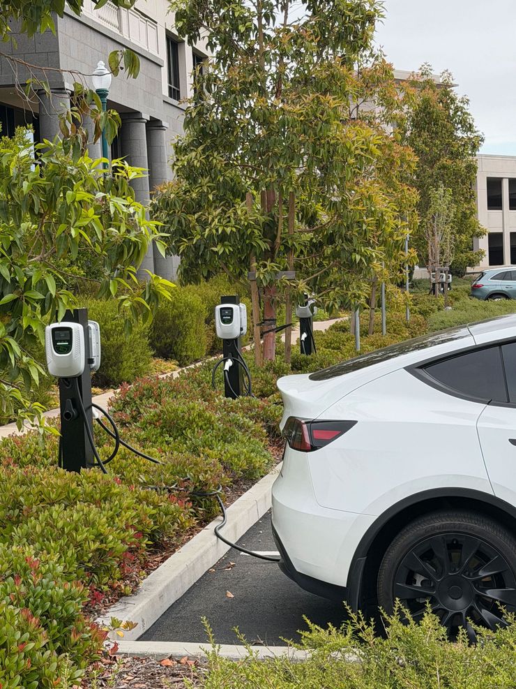 White electric car parked by outdoor EV charging stations beside a building and trees