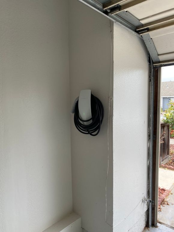 Open white electrical outlet cover on a garage wall near the door opening