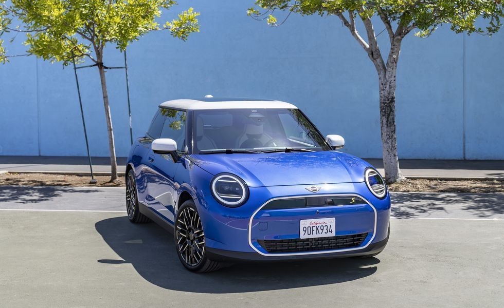 Blue Mini Cooper parked in front of a blue wall with trees casting shadows.