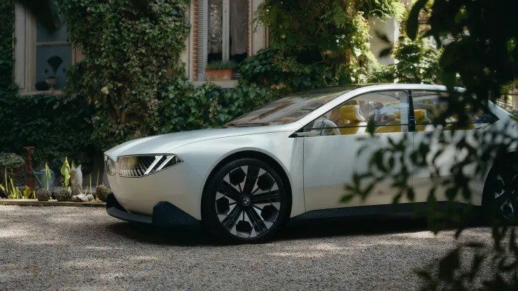 White sedan parked on a gravel driveway beside a house, partly framed by greenery