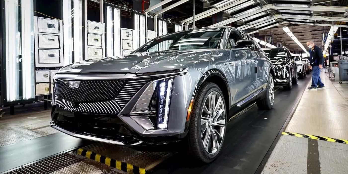 Silver concept car on an assembly line in a bright auto factory, with workers in the background