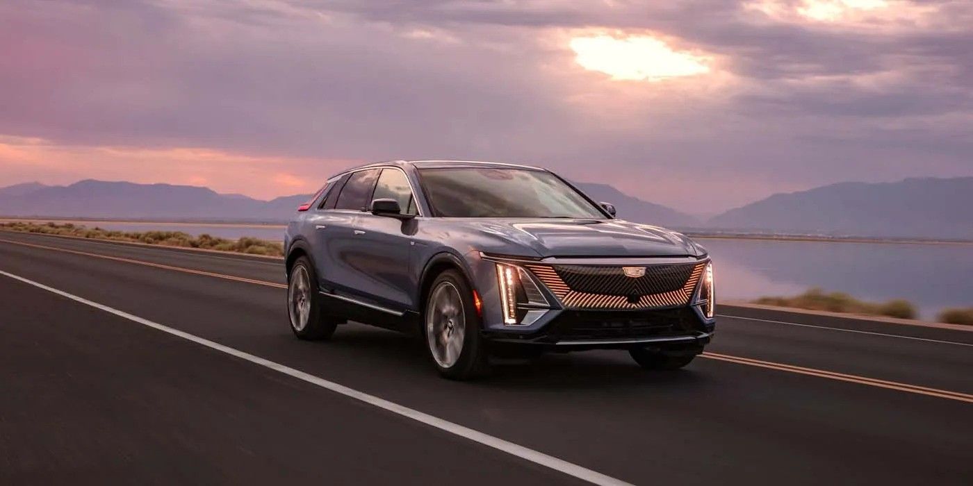 Silver SUV driving on a winding road at sunset beside a lake and mountains