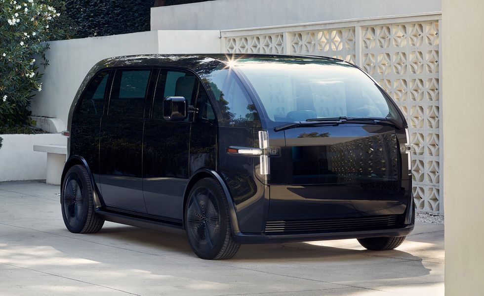 Black futuristic van parked in a driveway beside a patterned wall, front-left view