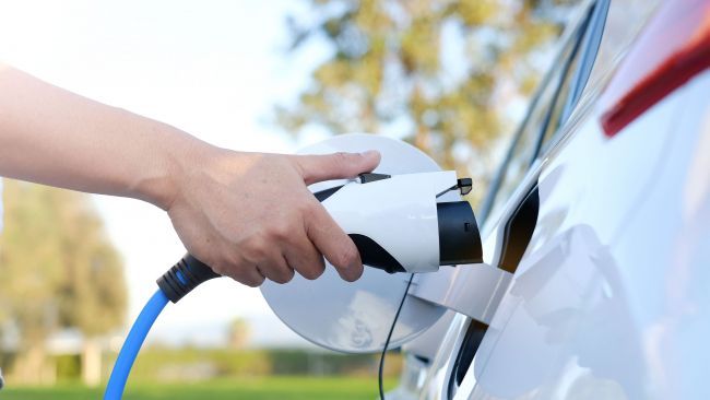Hand plugging a white EV charger into a car’s charging port outdoors