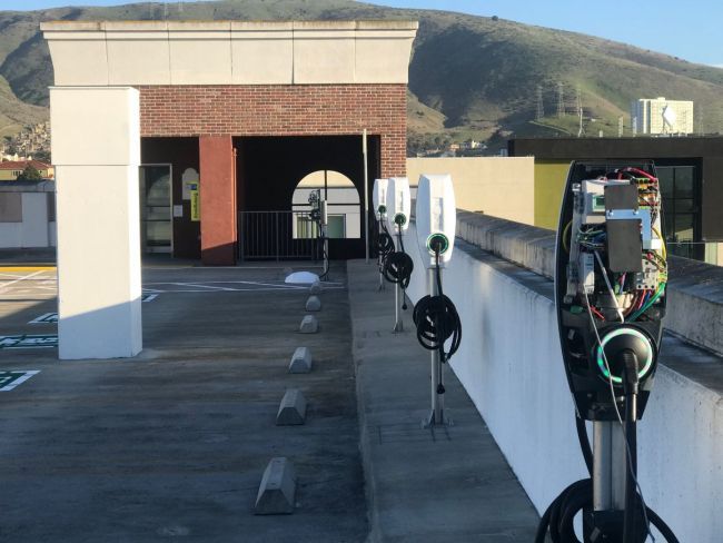 Rooftop parking lot with electric vehicle charging stations beside a low white wall and brick structure.