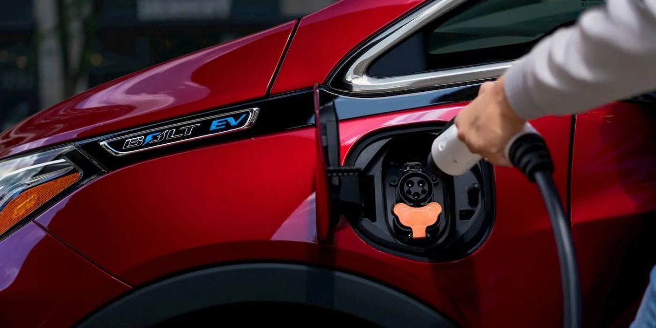 Hand plugging a charging connector into a red electric car’s charging port