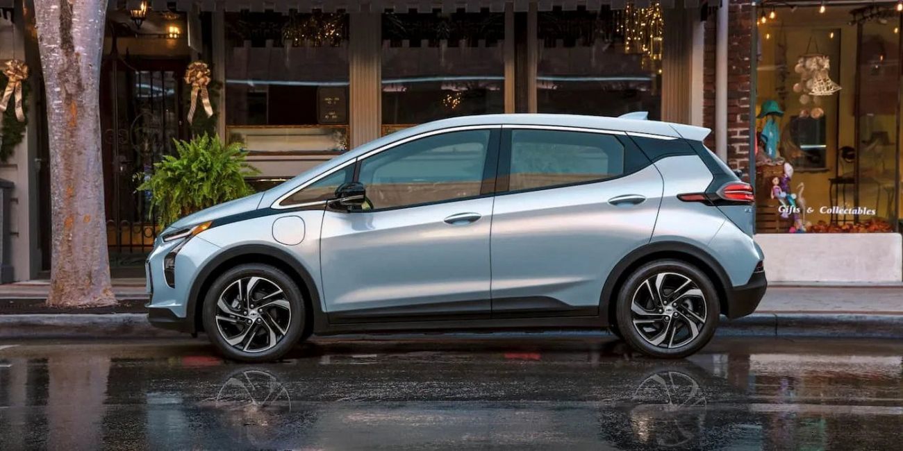 Silver hatchback parked on a wet city street in front of shops
