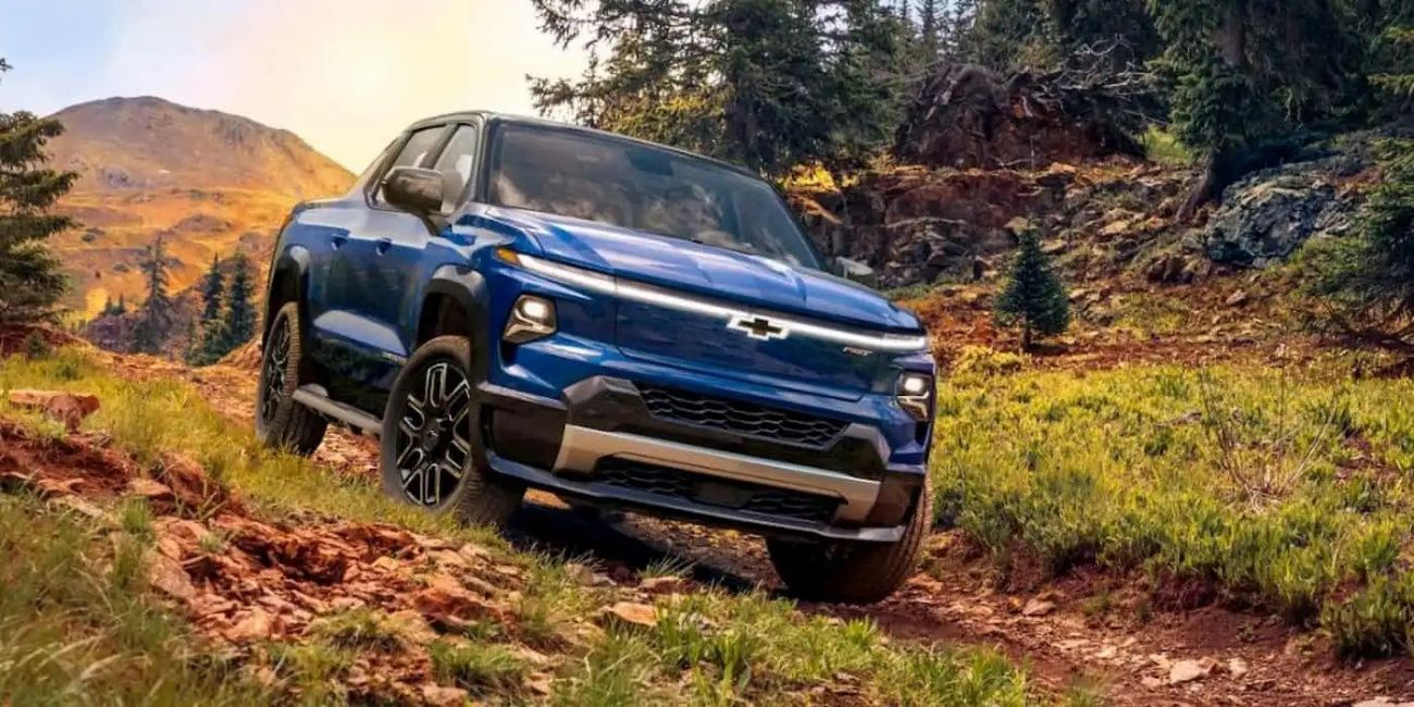 Blue pickup truck driving on a muddy dirt road in a rural hillside setting