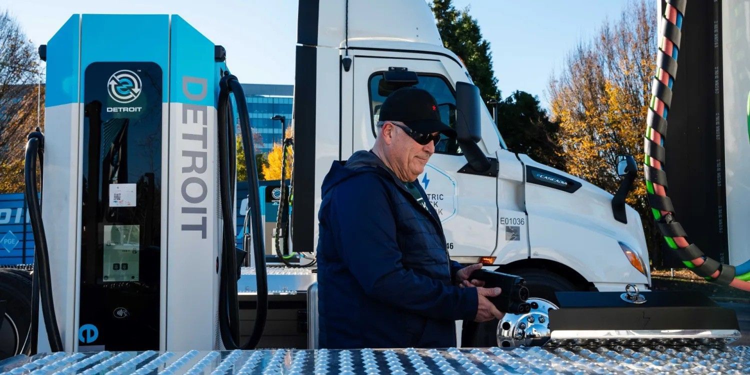 Driver standing beside a blue and white semi-truck charging at a roadside station