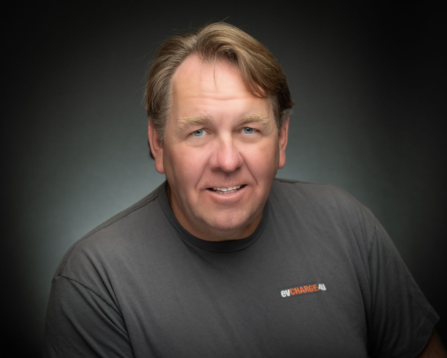 Studio portrait of a smiling man in a dark gray T-shirt against a black background