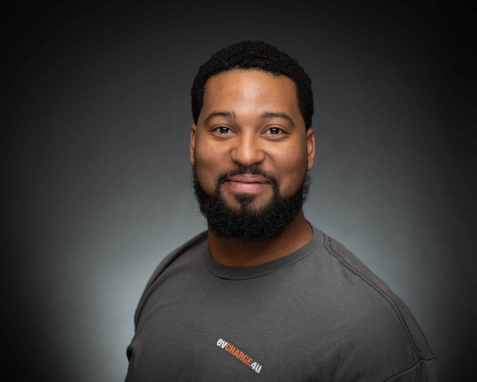 Portrait of a smiling person in a gray shirt against a dark gradient background