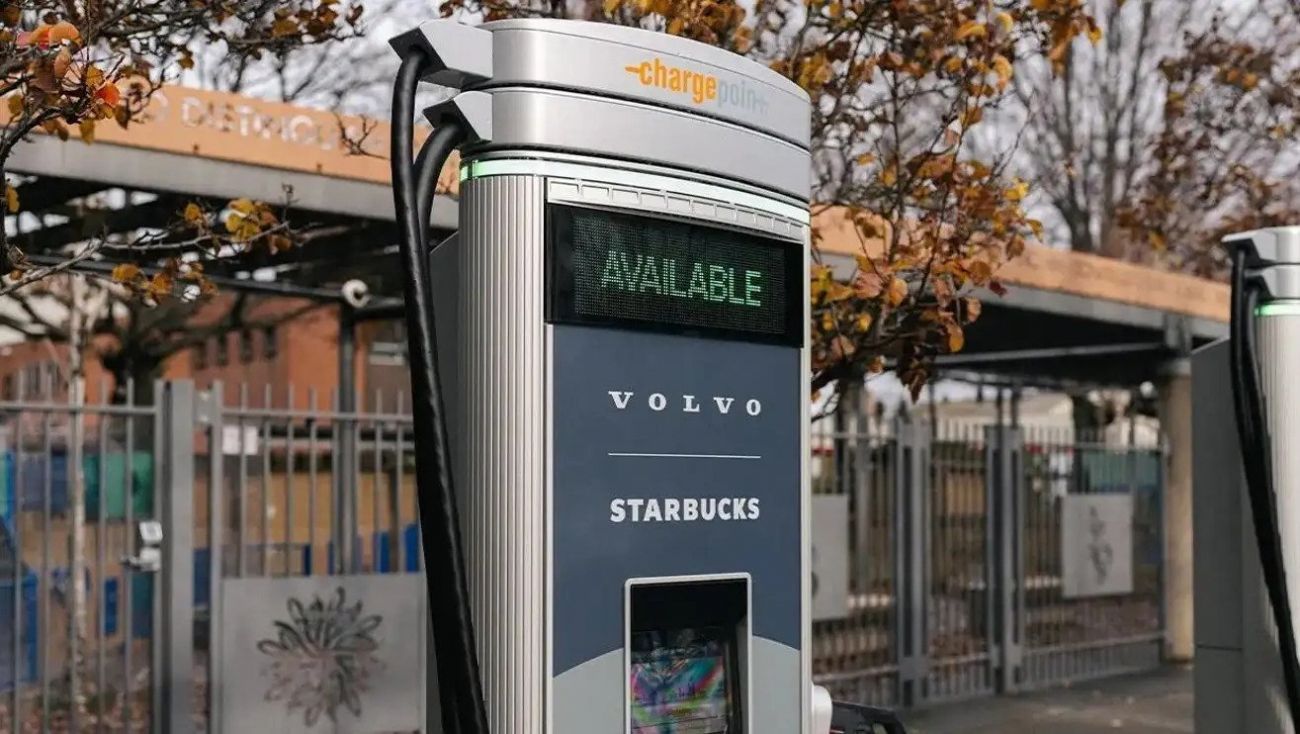 Street kiosk with a digital ad for Volvo and Starbucks in front of a fenced transit stop