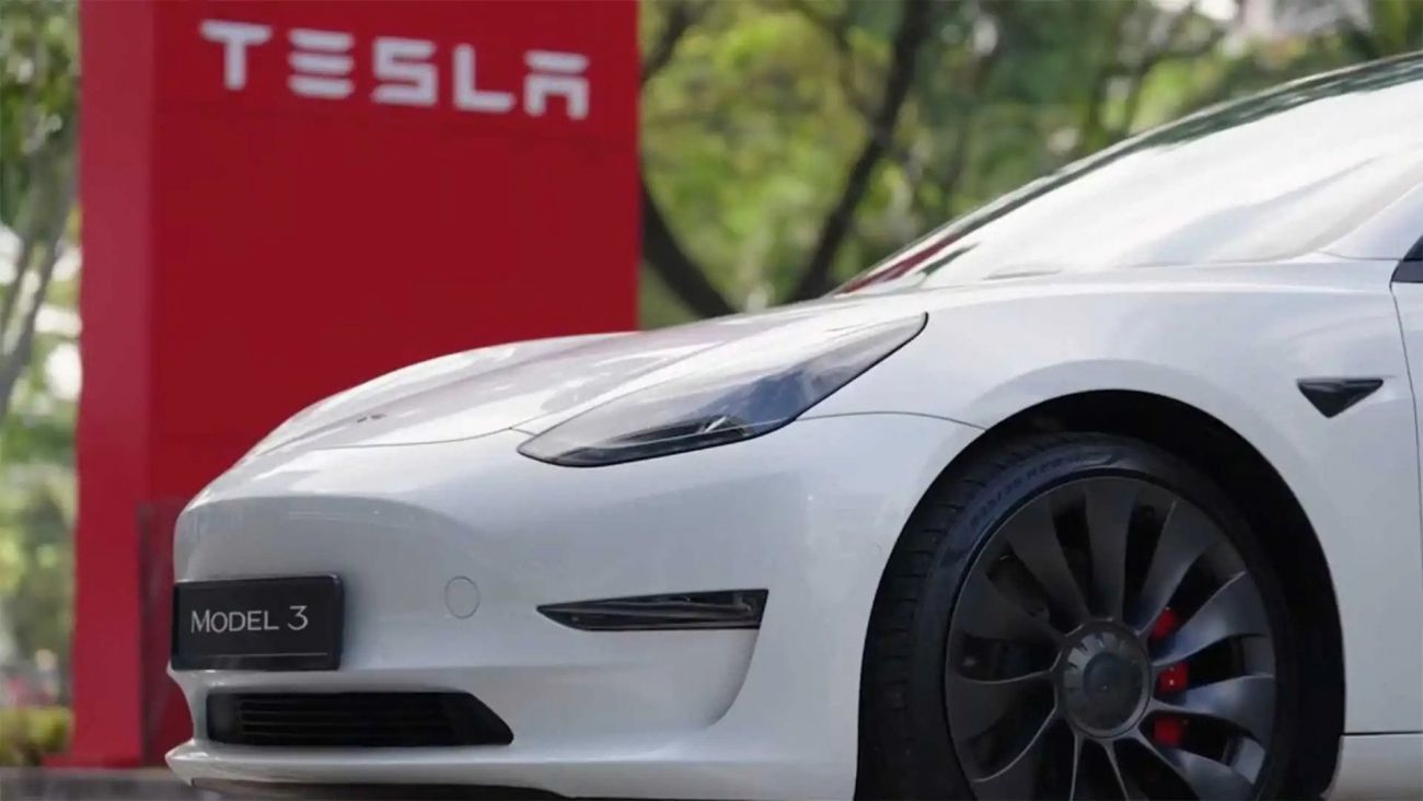 White Tesla Model 3 parked beside a red Tesla sign outdoors