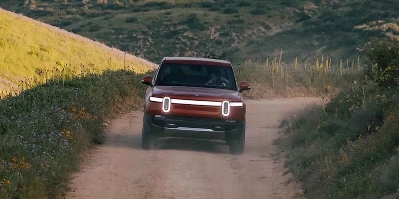 Red SUV driving on a dusty dirt road between green hills.