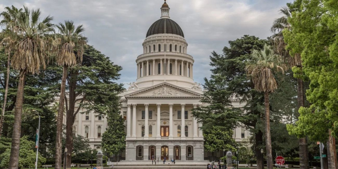 California State Capitol building framed by palm trees on a cloudy day