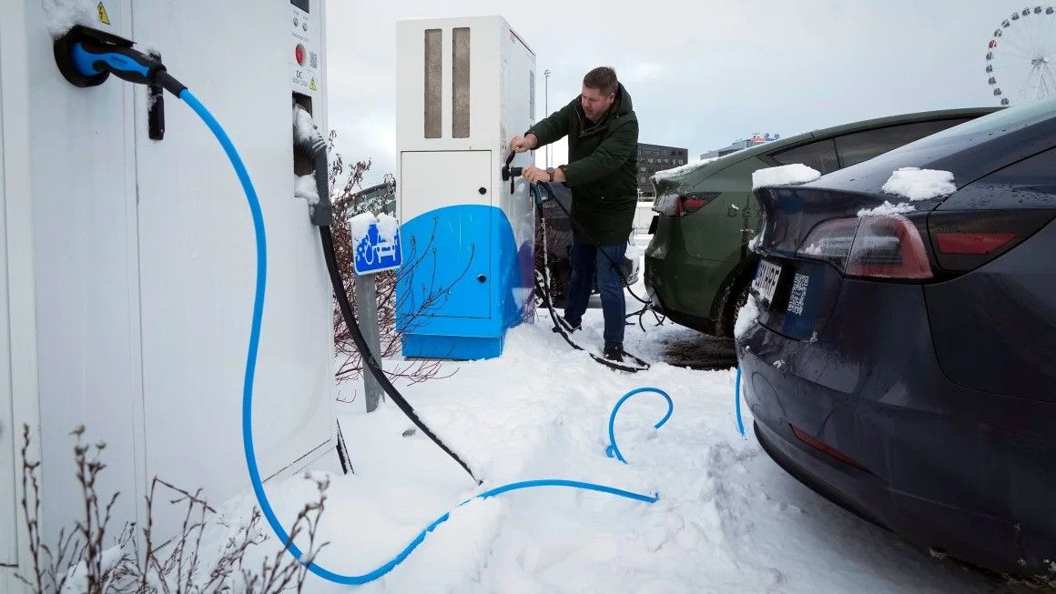 Person charging an electric car at a snowy outdoor charging station