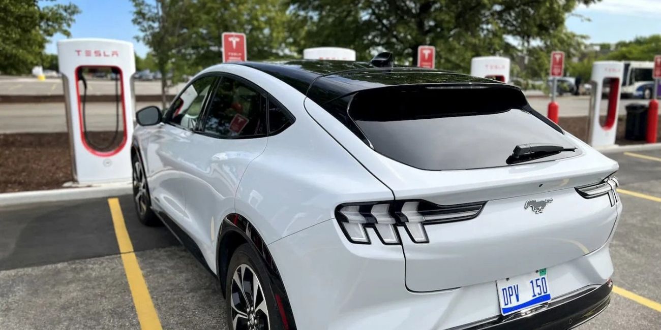 White sports SUV parked at a Tesla charging station, rear three-quarter view on a sunny day