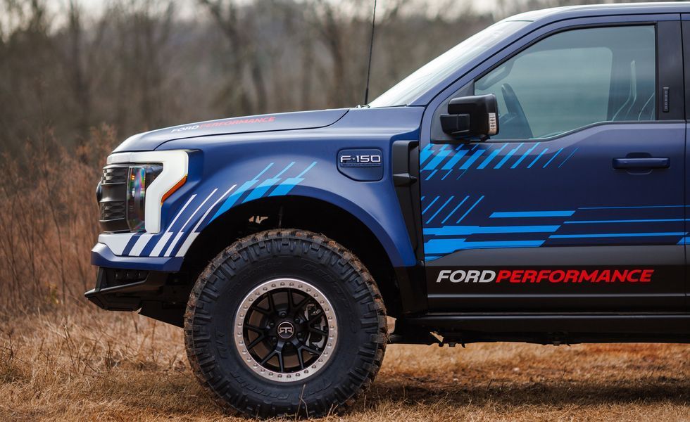 Blue Ford Performance pickup truck with off-road tires on a dirt road, side view