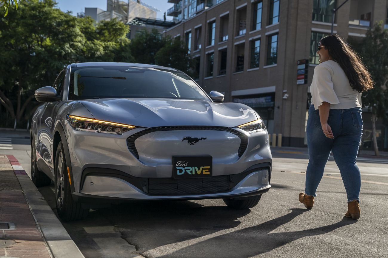 Electric car parked on a city street as a woman walks past nearby.