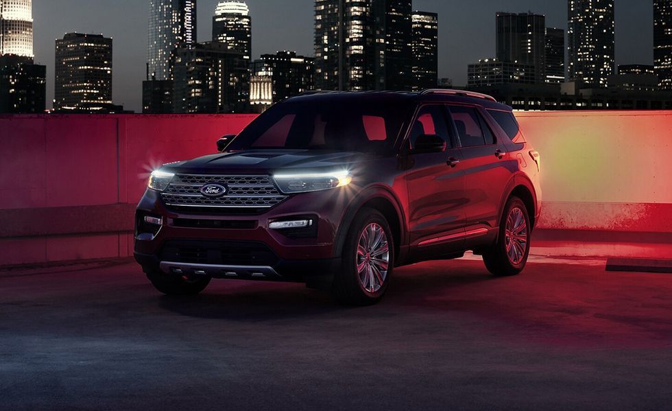 Red SUV parked on a rooftop at night with a lit city skyline in the background.
