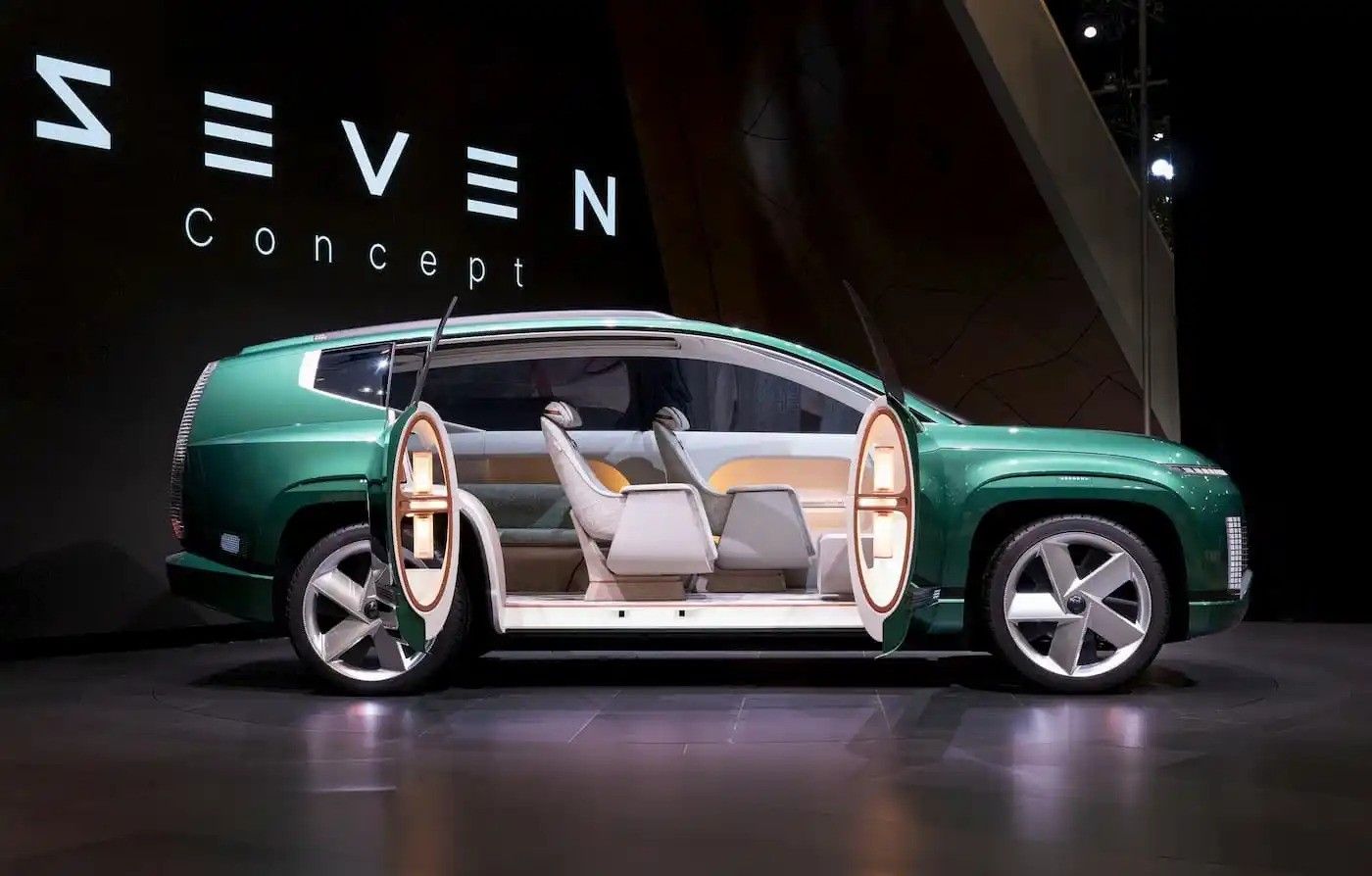 Green concept car with gullwing doors open on a stage at a SEVEN design event