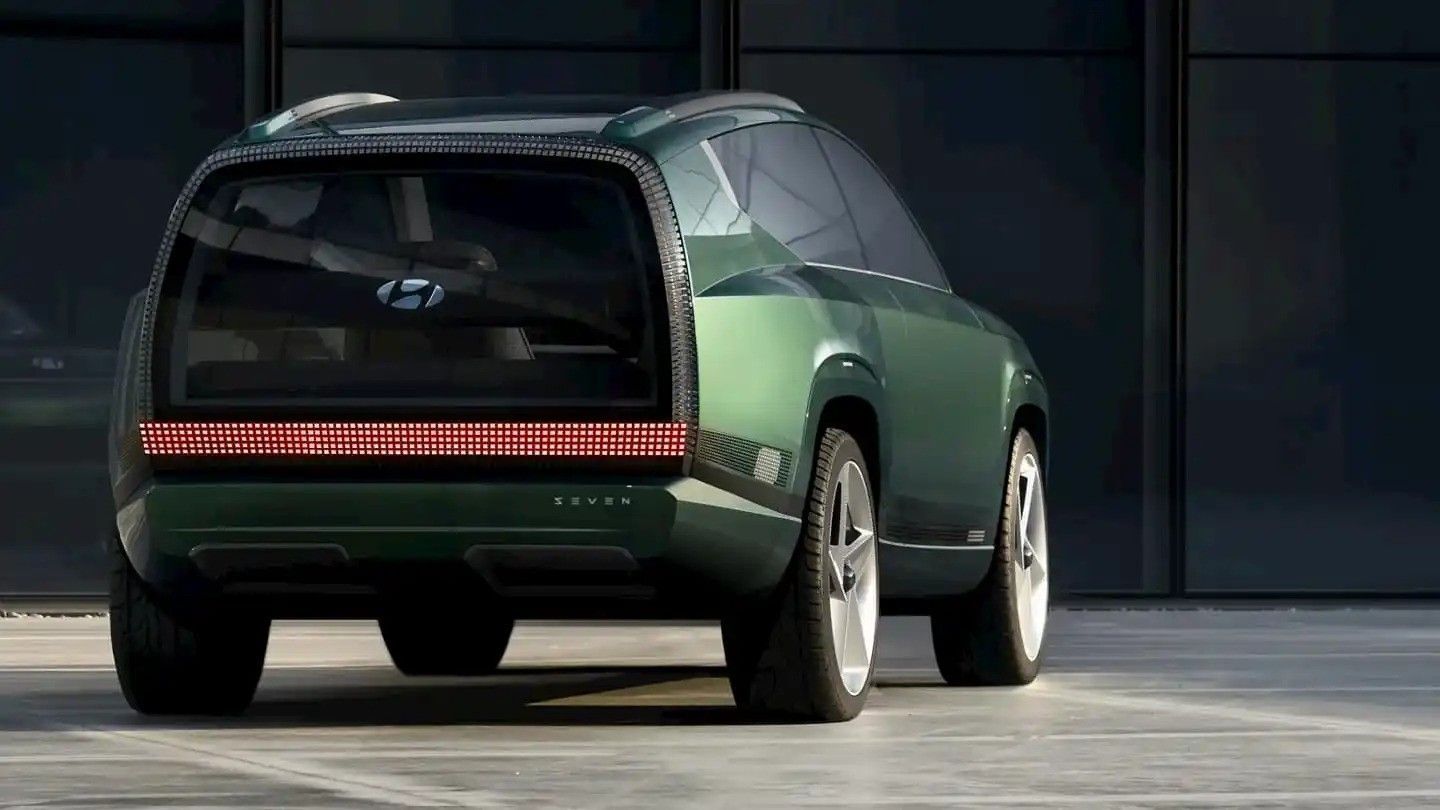 Green concept SUV shown from the rear in a dark studio setting with a full-width red taillight strip