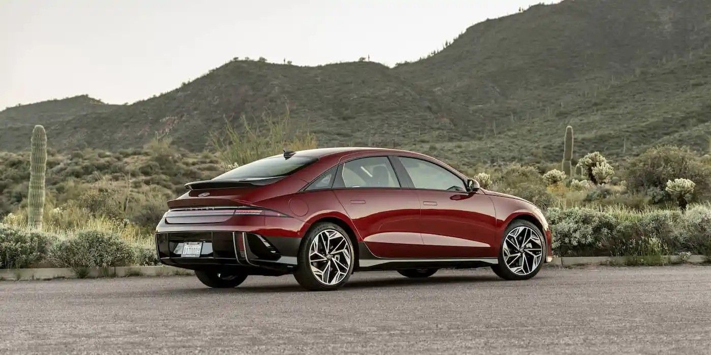 Red sports coupe parked on a road with mountains and greenery in the background