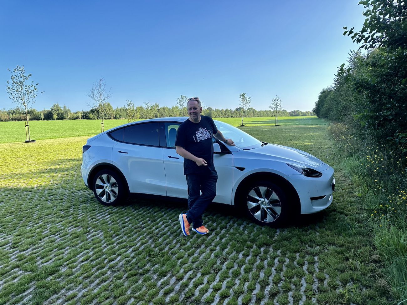 Person standing beside a white SUV on a grassy field under a clear blue sky.