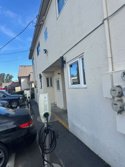 Narrow side view of a white building with parked cars, a door, window, and electric meters along the wall