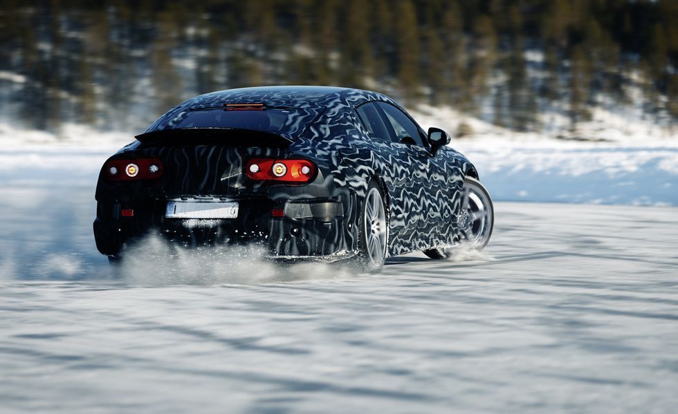 Black sports car drifting through snow, kicking up a white spray on a wintry road