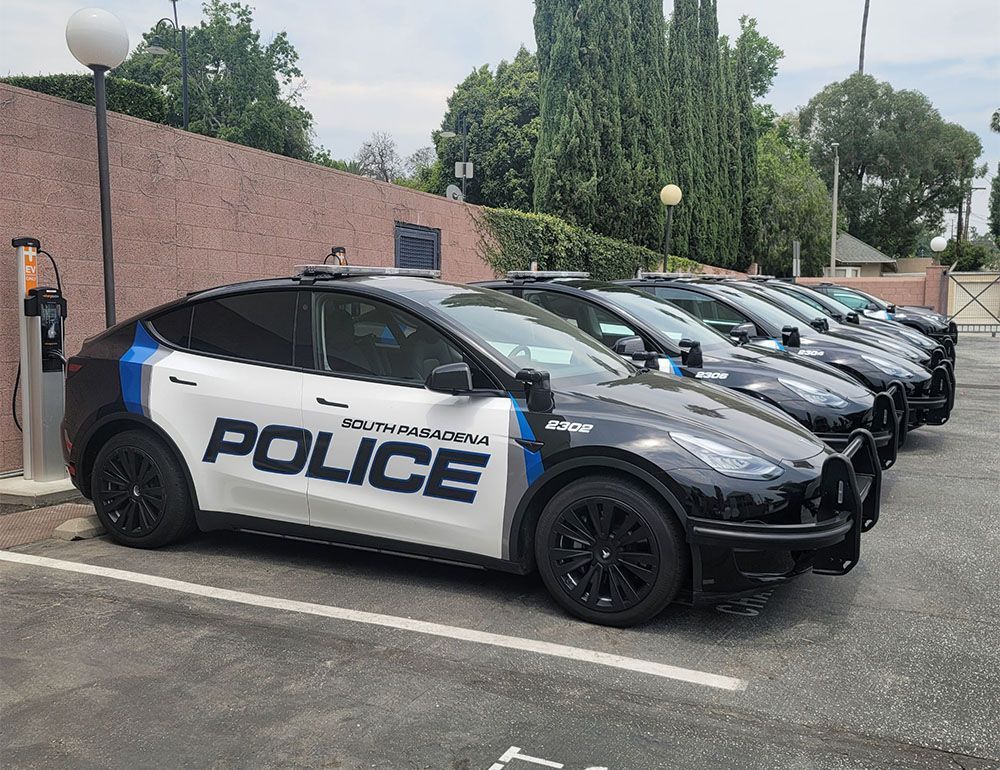 Row of black-and-white police cars parked beside a brick wall