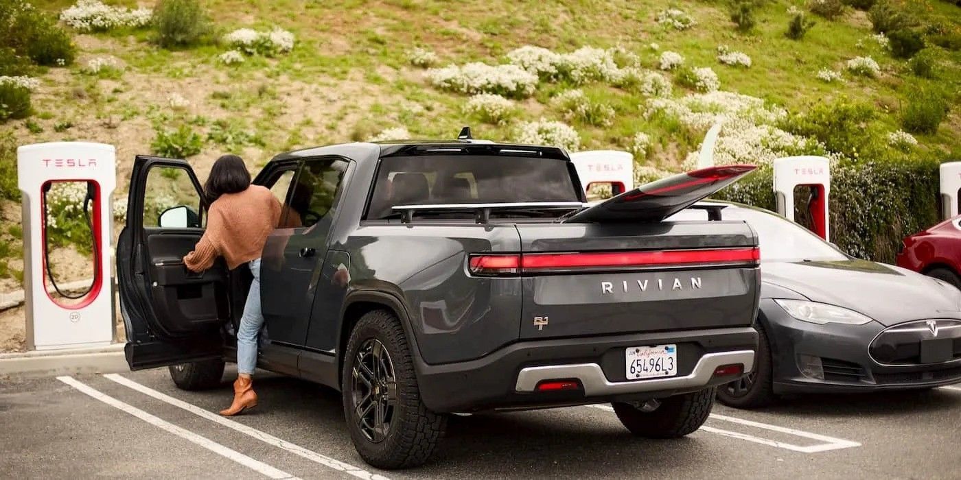 Black Rivian SUV charging at a Tesla Supercharger, with a person stepping out beside it.